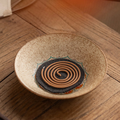 Vintage ceramic incense dish with fireproof mat holding a burning spiral coil incense, retro aromatherapy diffuser