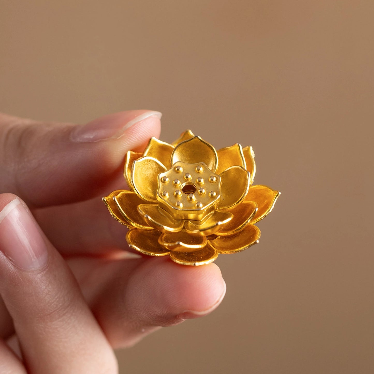 Close-up of hand holding a golden brass lotus flower incense stick holder, intricate metal accessory for incense trays.