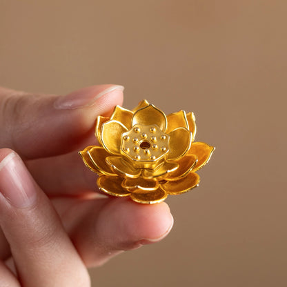 Close-up of hand holding a golden brass lotus flower incense stick holder, intricate metal accessory for incense trays.