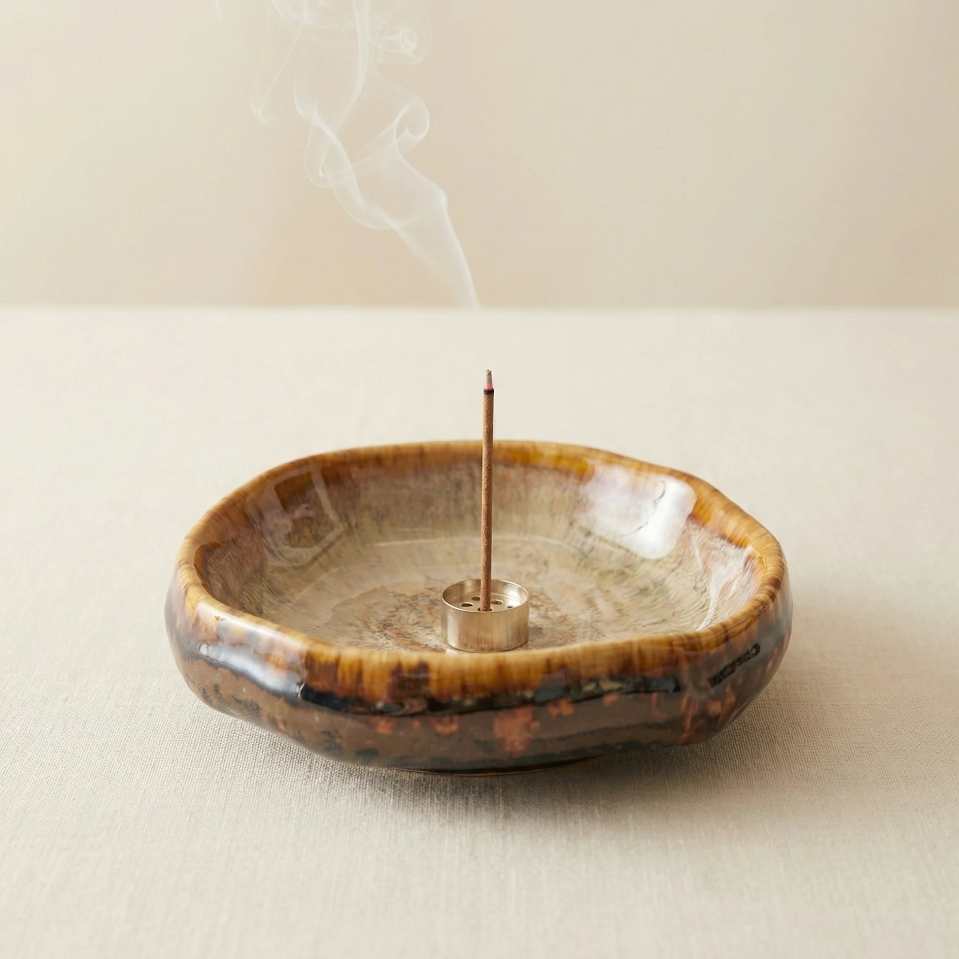 Burning incense stick in a rustic kiln-altered ceramic holder with wisps of smoke, creating a peaceful zen atmosphere