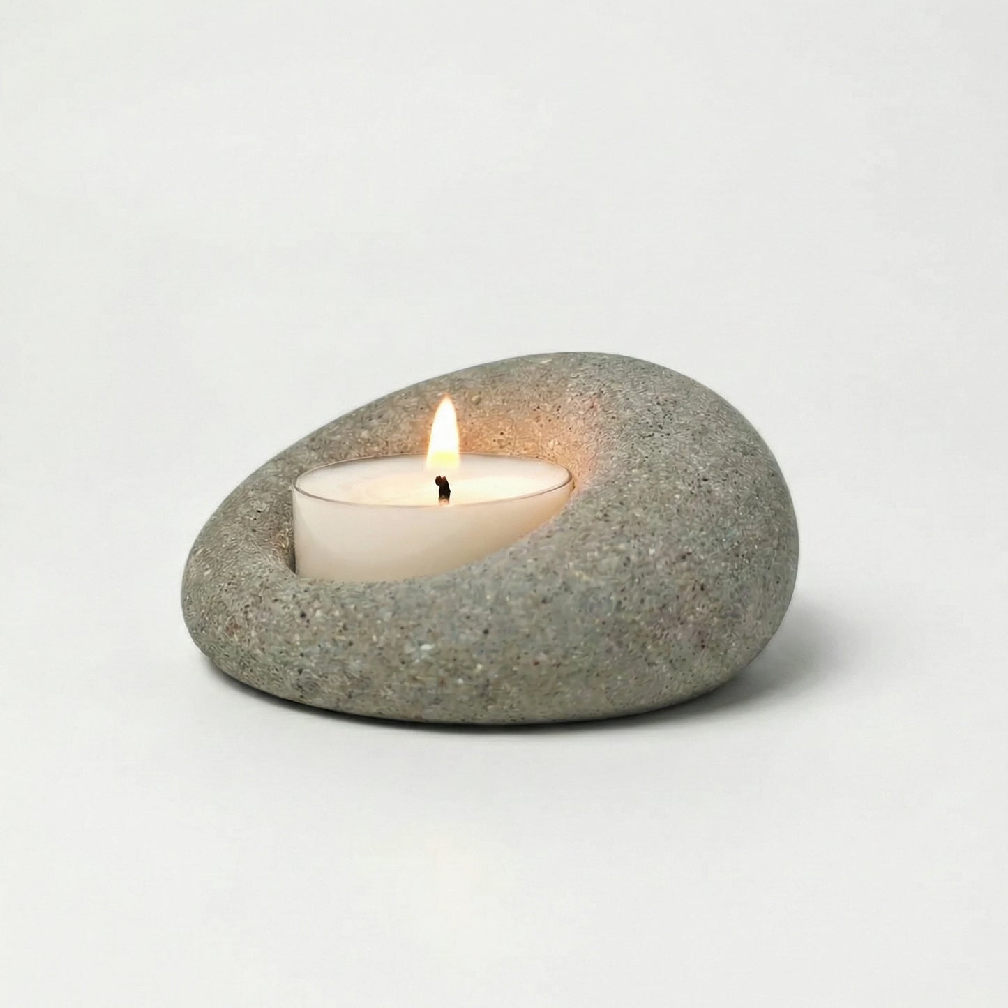 Minimalist natural stone tealight holder with a lit candle, wabi-sabi home decor accessory on a white background