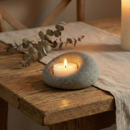 Artisanal river rock candle holder on a rustic wooden table with dried eucalyptus, creating a cozy zen atmosphere.