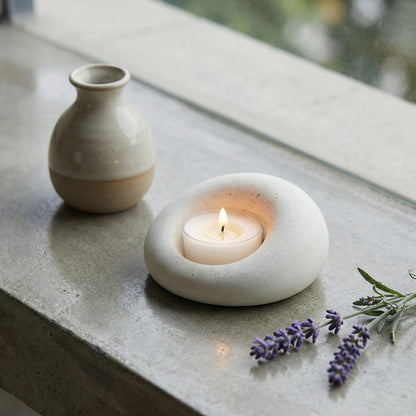 Smooth white stone candle holder on a concrete window sill next to a ceramic vase and lavender sprigs.