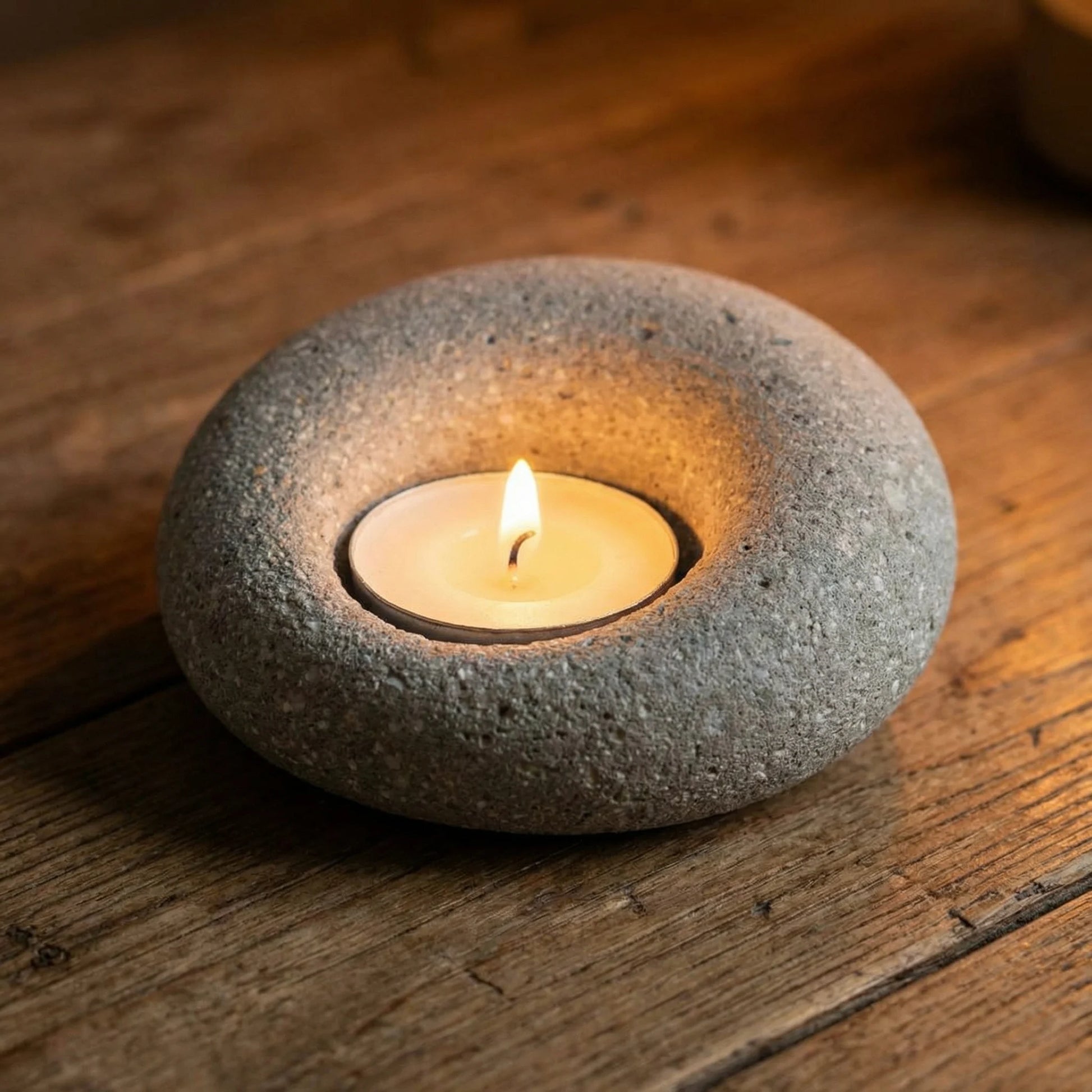 Close-up of a lit tealight inside a textured natural stone holder, warm golden glow on a wooden surface.