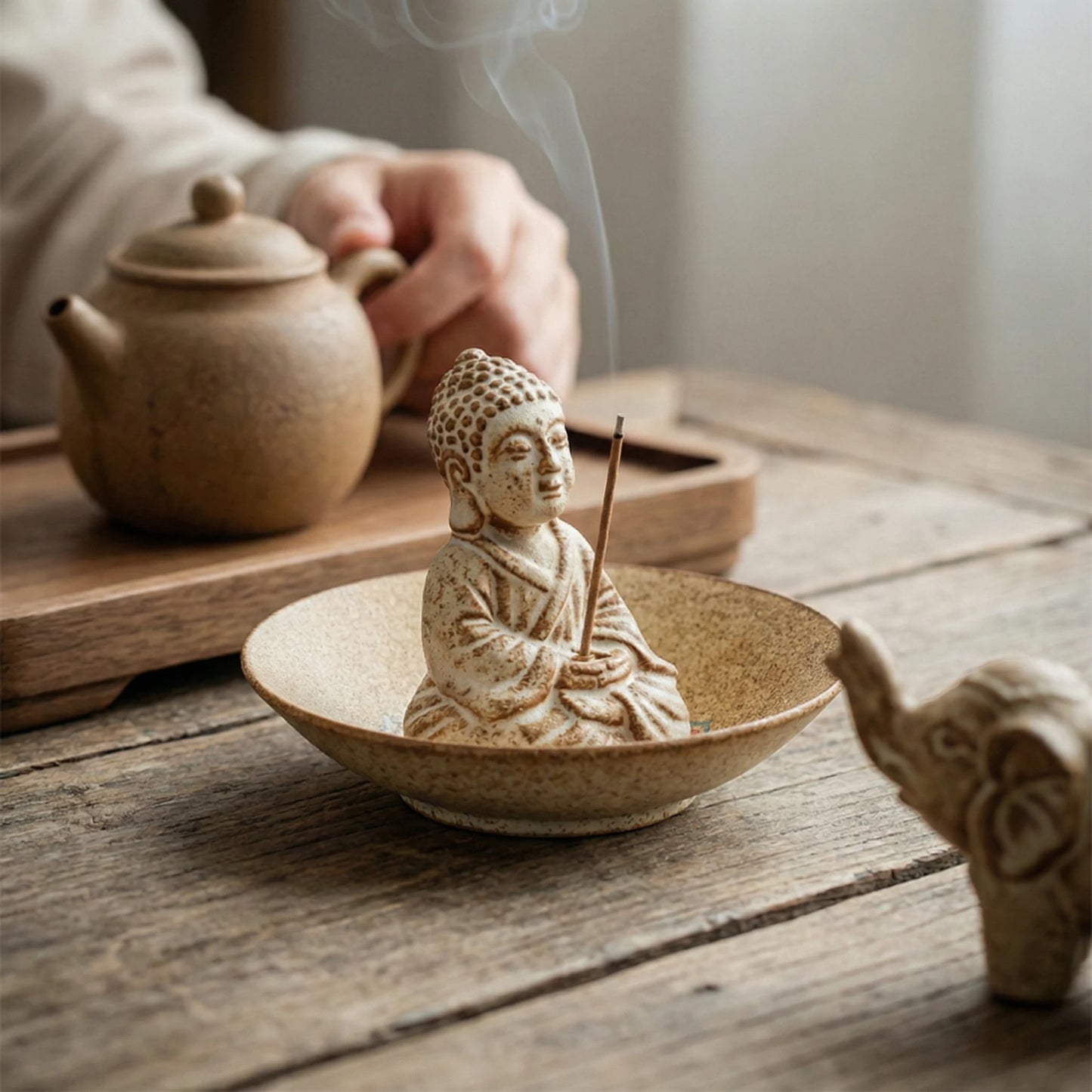 Relaxing tea ceremony setting with ceramic Buddha incense burner in a bowl and tea pot background
