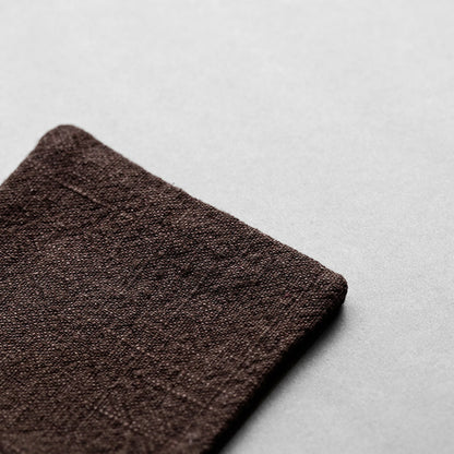 Extreme close-up of a dark chocolate brown linen coaster, showcasing the intricate breathable fabric texture and artisanal quality
