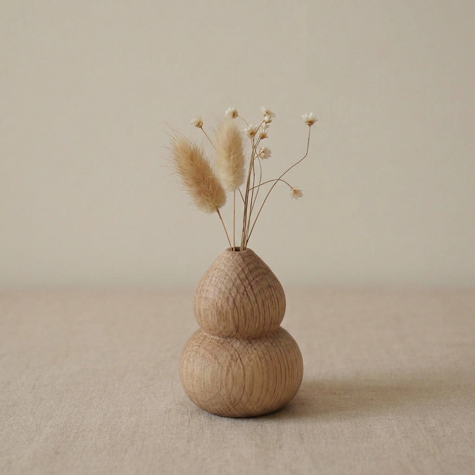 Miniature gourd-shaped white oak wood vase with dried bunny tail grass on a neutral linen background