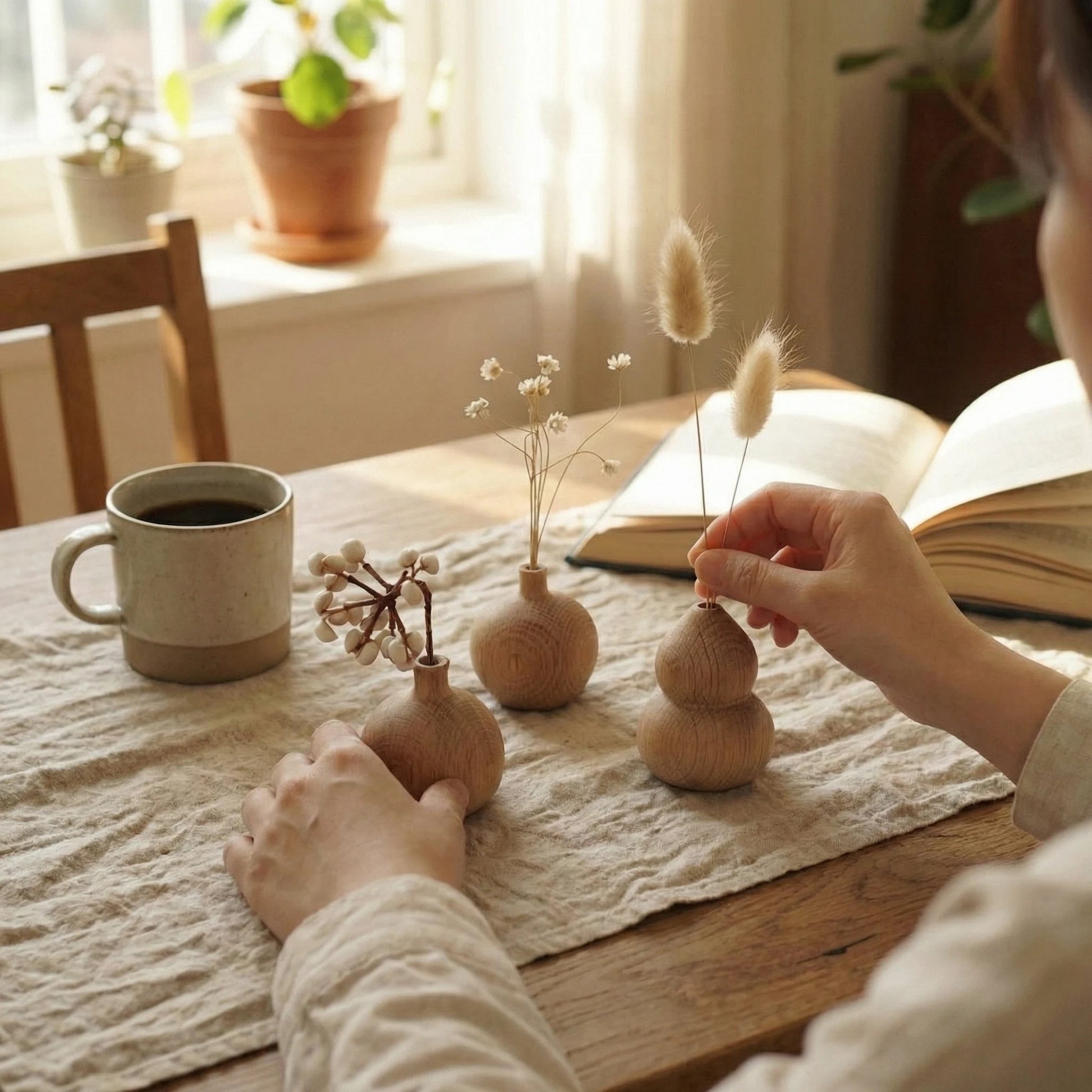 Close-up of three wabi-sabi style white oak bud vases on a textured linen table runner with a coffee mug.