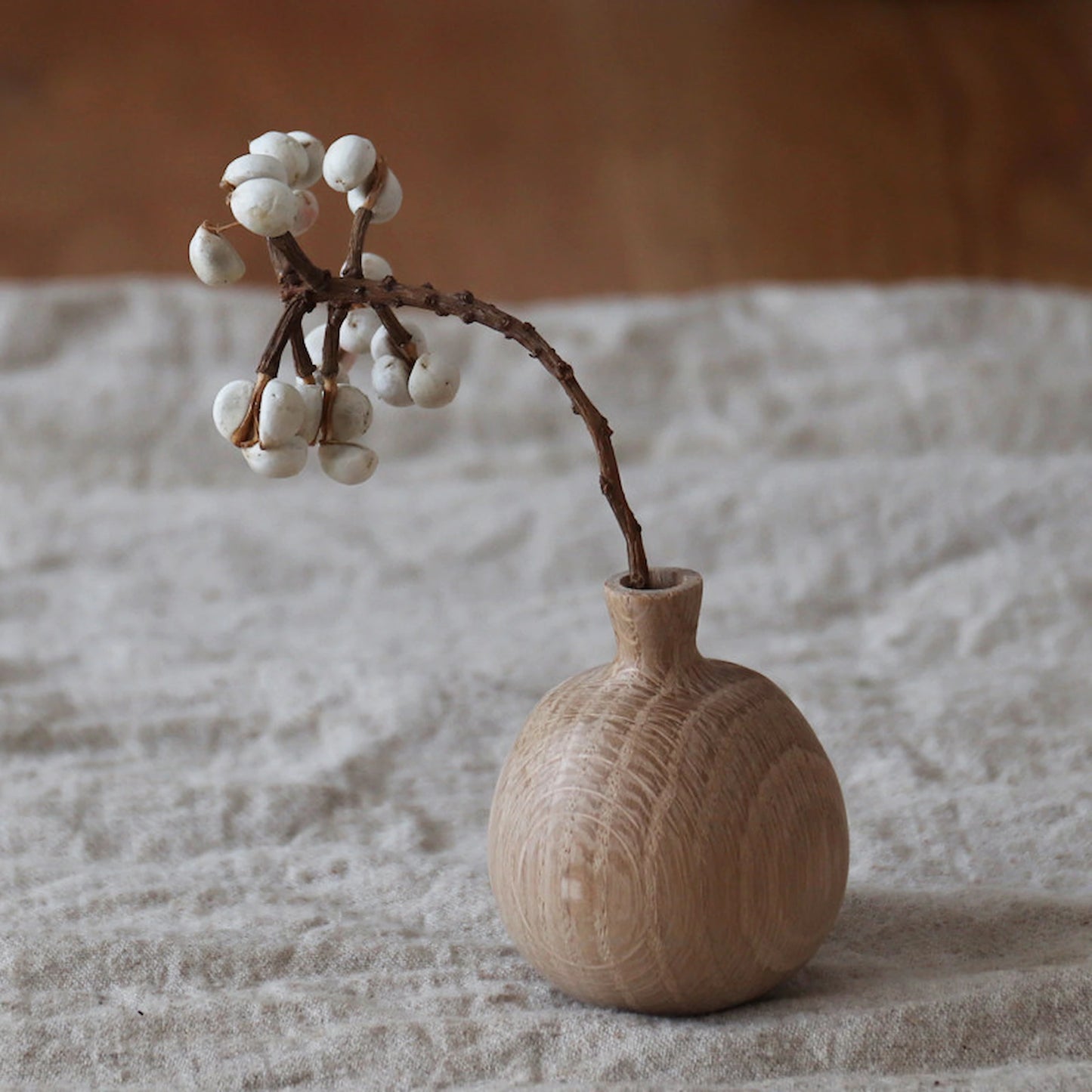 Lifestyle shot of a person arranging dried flowers in mini white oak vases on a cozy wooden dining table.