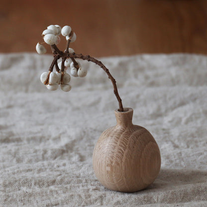 Lifestyle shot of a person arranging dried flowers in mini white oak vases on a cozy wooden dining table.